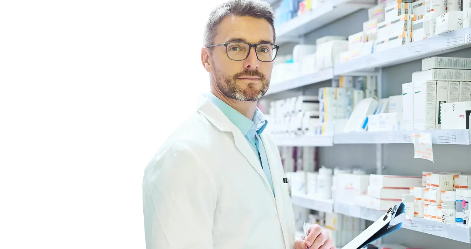 Pharmacist in a white coat in front of pharmacy shelves